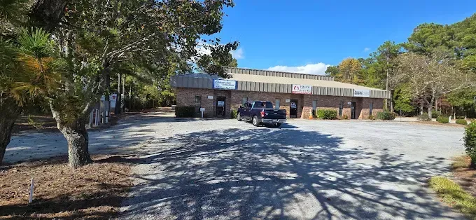 A one-story brick building with a pickup truck parked out front on a gravel lot; blue sky overhead.