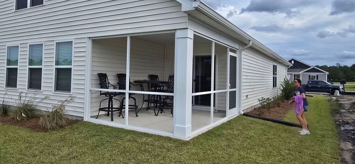 Screened-in porch on a white house with a table and chairs, a person and child on the lawn.