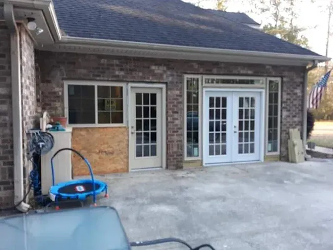 Exterior of a brick building with doors and windows. Concrete patio area, blue trampoline, and American flag visible.