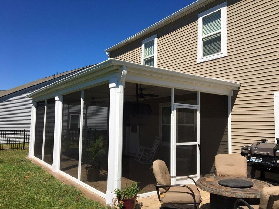 Screened-in porch attached to a house with beige siding, a patio, and outdoor furniture.
