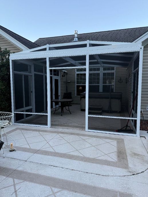 White screened-in patio attached to a house with an outdoor seating area.