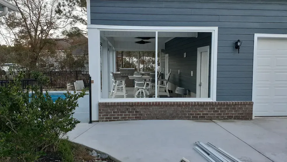 Patio with sliding glass doors, blue siding, brick base. Pool and backyard visible through doors.