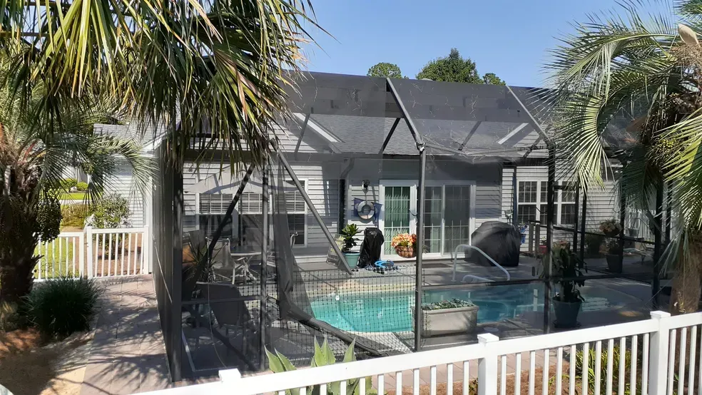Backyard pool enclosed by a screened-in structure, with palm trees and a white fence in view.
