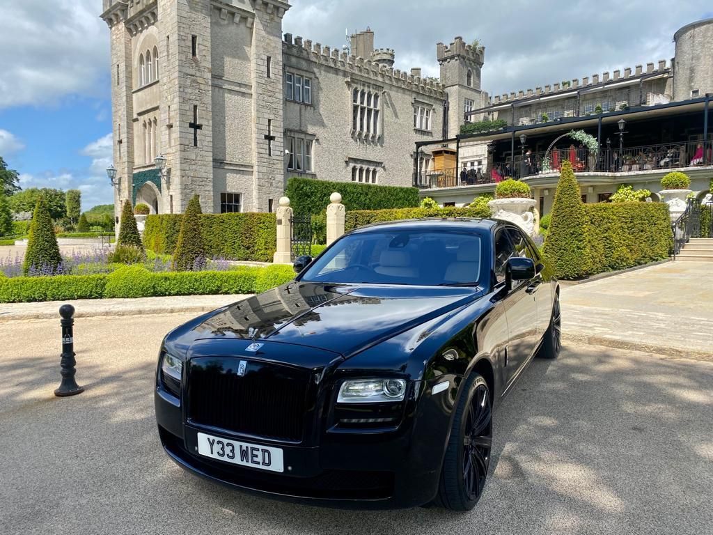 Black Rolls-Royce parked in front of a stone castle with manicured gardens