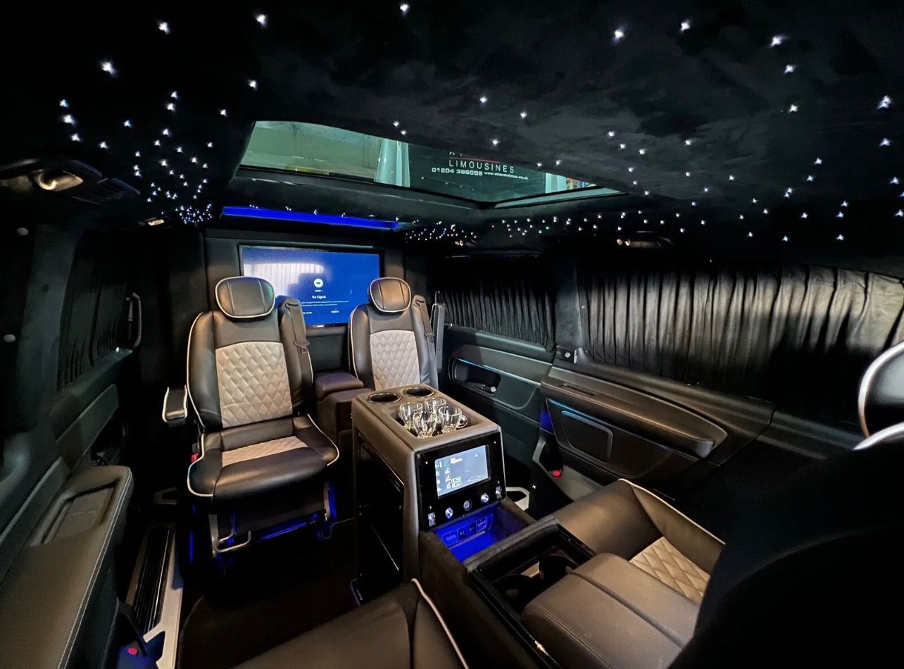 Luxurious limousine interior with black leather seats, starry ceiling lights, and a blue-lit console