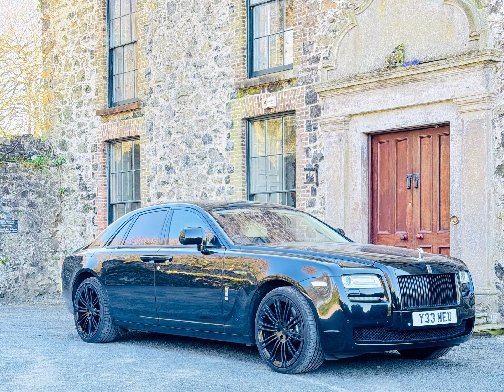 Black luxury sedan parked beside an old stone building with wooden doors.