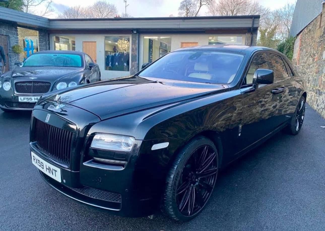 Black Rolls-Royce coupe parked outside a building on a wet driveway