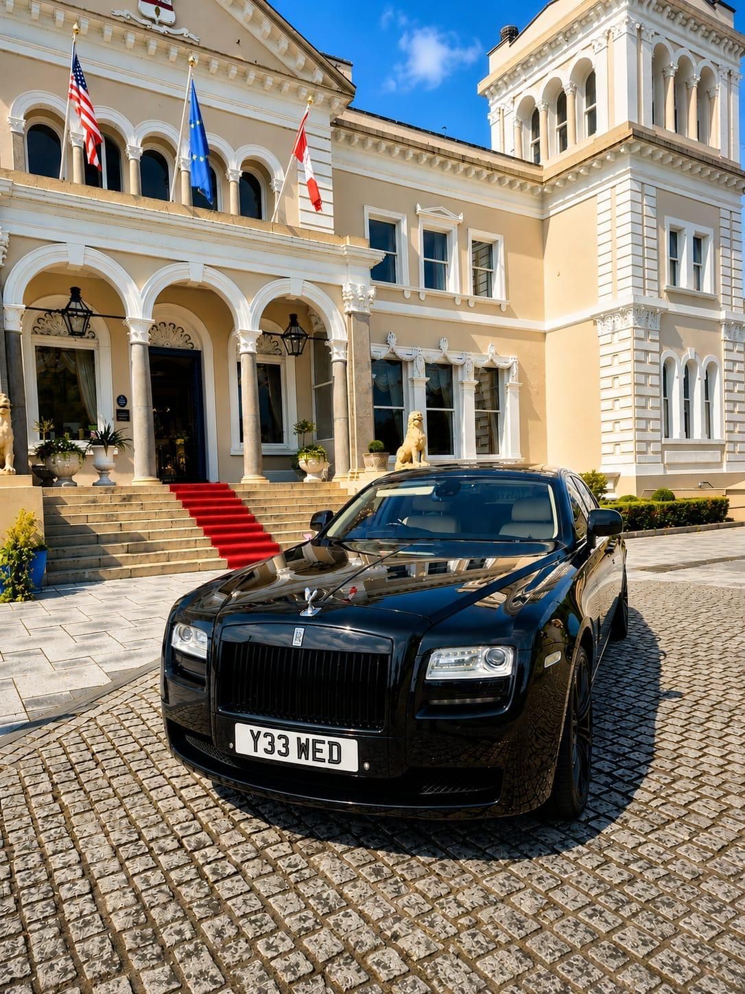 Black luxury car parked in front of a grand hotel with a red carpet and arched entrance