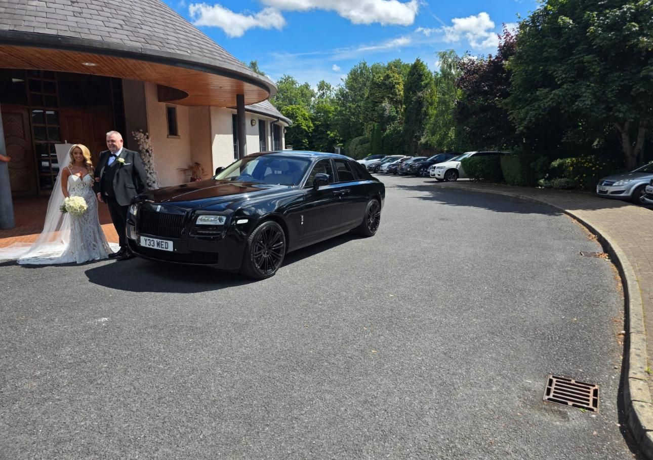 Bride and groom by a black car outside a building on a sunny day