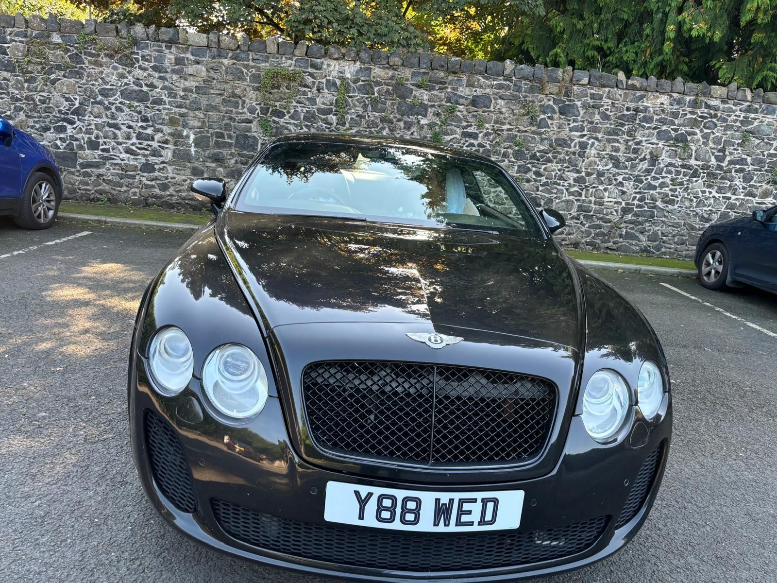 Black Bentley convertible parked in a lot, front view with UK license plate Y88 WED.
