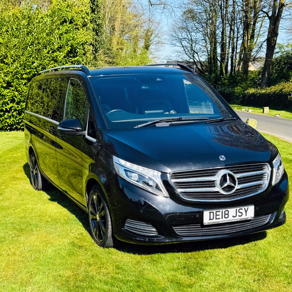 Black Mercedes van parked on grass beside a tree-lined road in bright sunlight