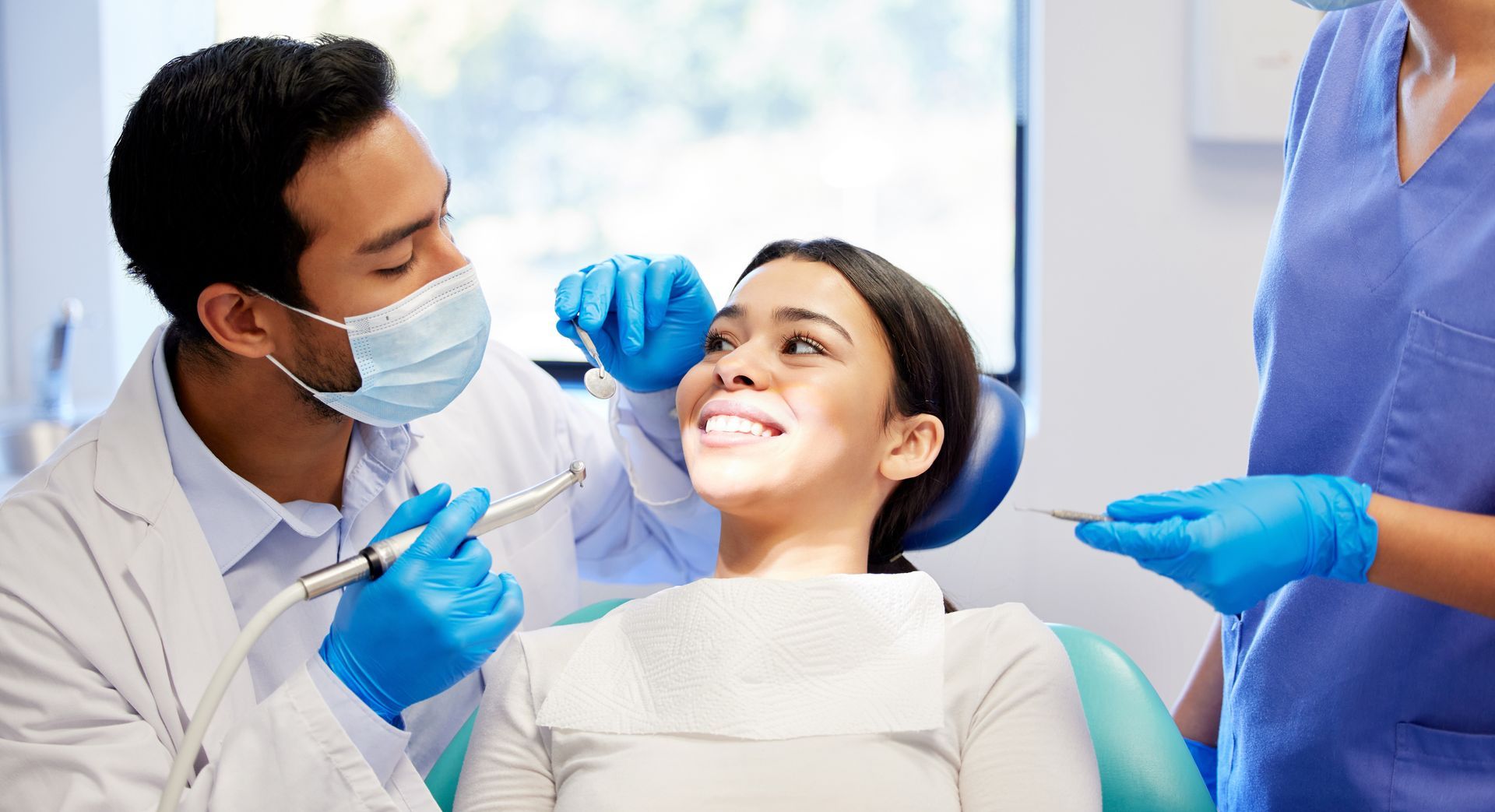 Dentist examining a patient during a routine dental checkup with an assistant nearby.