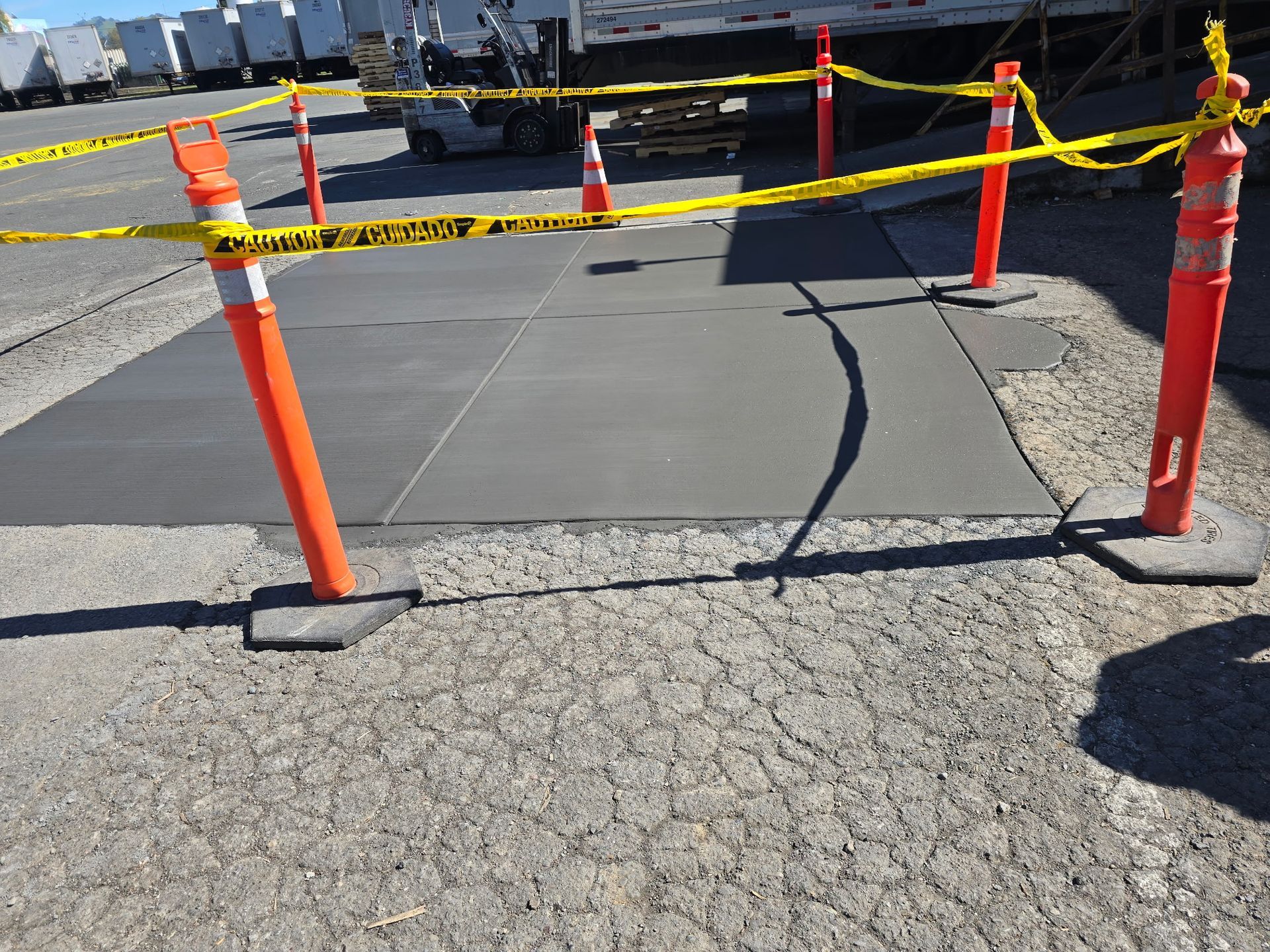 Orange cones and yellow caution tape blocking a cracked concrete path near a waterfront.