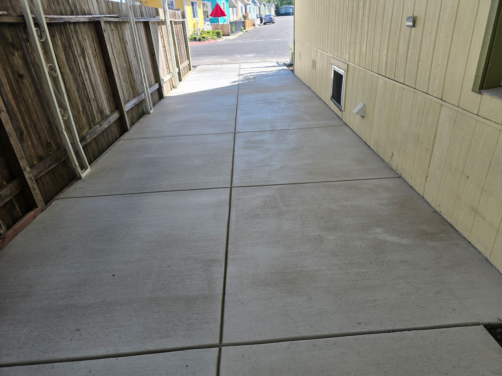 Empty concrete walkway between a wooden fence and beige building, leading toward a street.