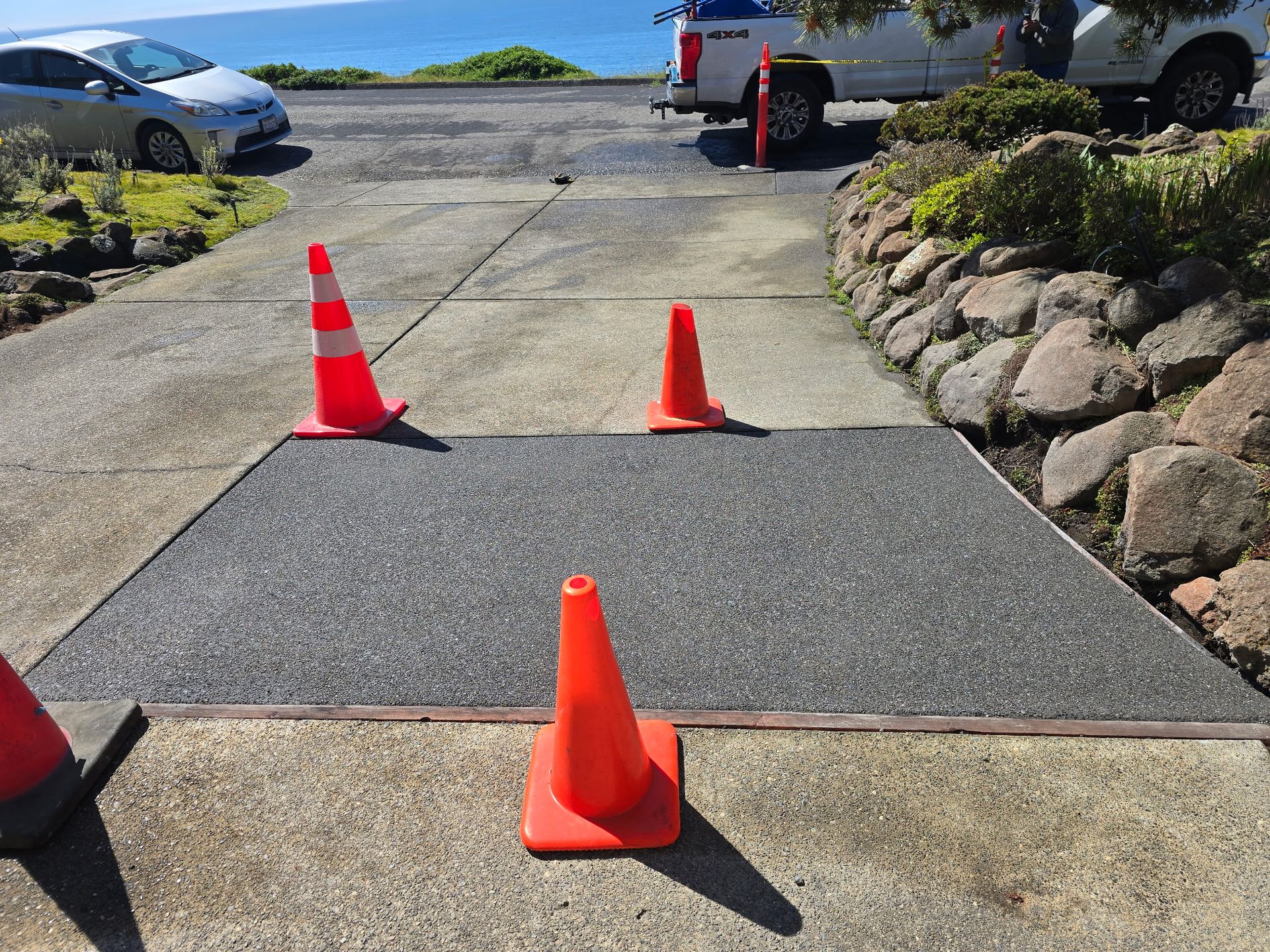 Orange traffic cones marking a dark mat on a driveway by the road and parked cars