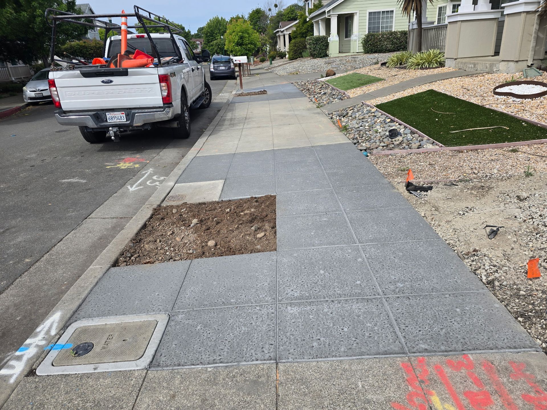 Sidewalk under repair beside a residential street, with a pickup truck parked at the curb.