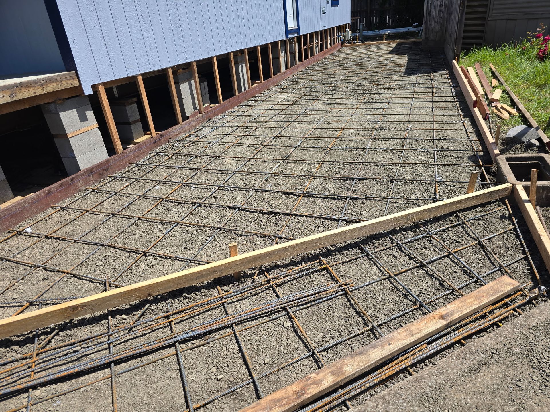 Concrete slab under construction beside a building, with rebar grid and wooden braces.