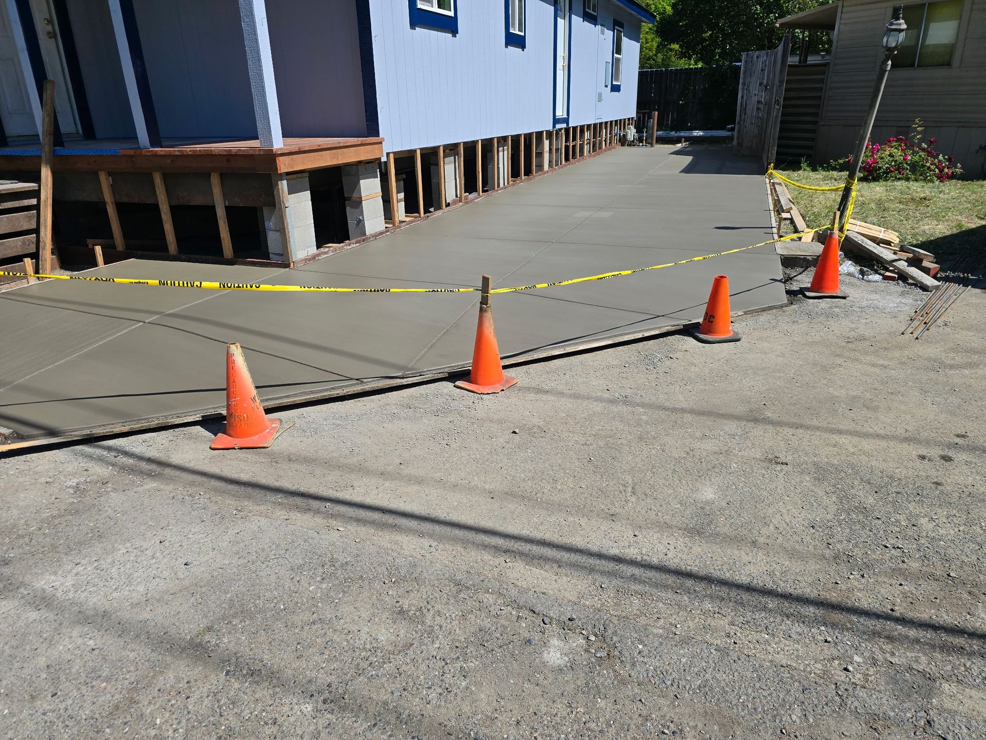 Orange cones and caution tape blocking a damaged sidewalk beside a blue building