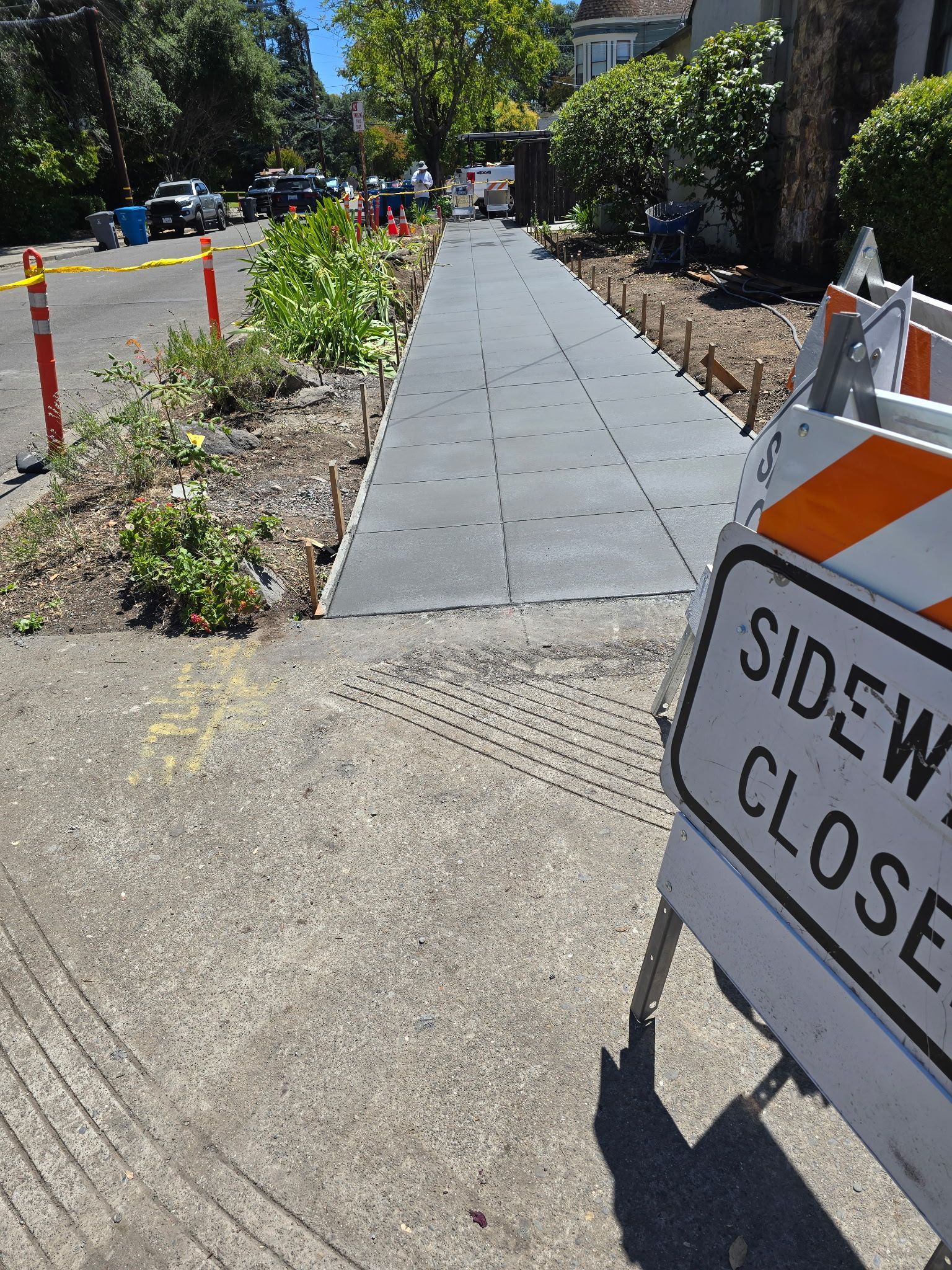 Sidewalk under repair with closed-sidewalk sign and orange barricade along a sunny street