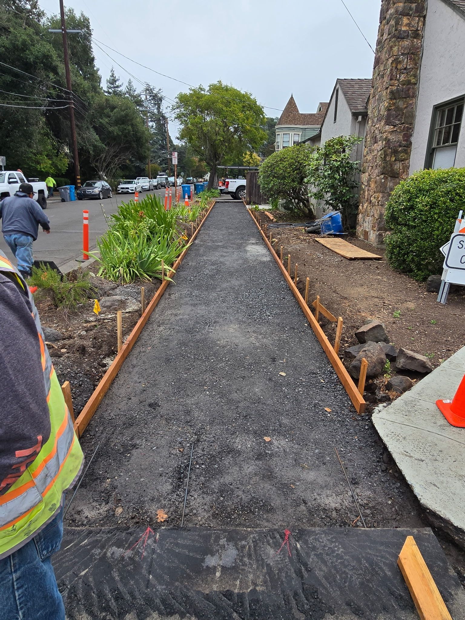 Garden walkway under construction with gravel path, orange edging, and workers nearby