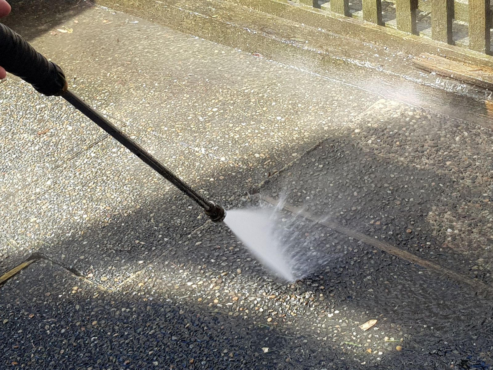 Person using a pressure washer, cleaning a dark, textured surface outdoors.