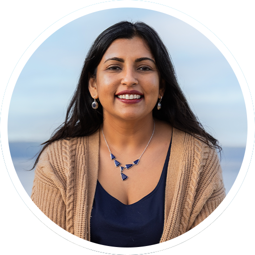 Smiling woman in a beige cardigan and navy top against a soft blue sky background