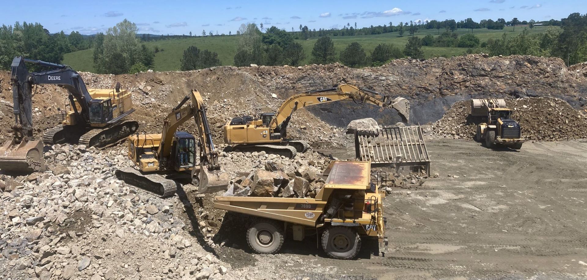 A group of construction vehicles are working in a dirt field.