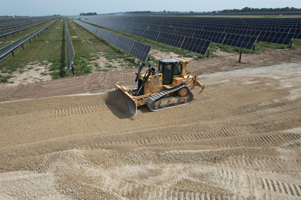 A bulldozer is moving dirt in a field of solar panels.