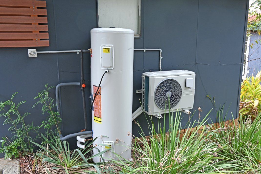 A Water Heater is Attached to the Side of a Building Next to an Air Conditioner — TCP Plumbing in Bonalbo, NSW
