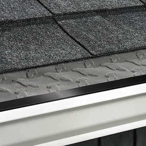 Hand removing wet leaves from a gutter beside a roof