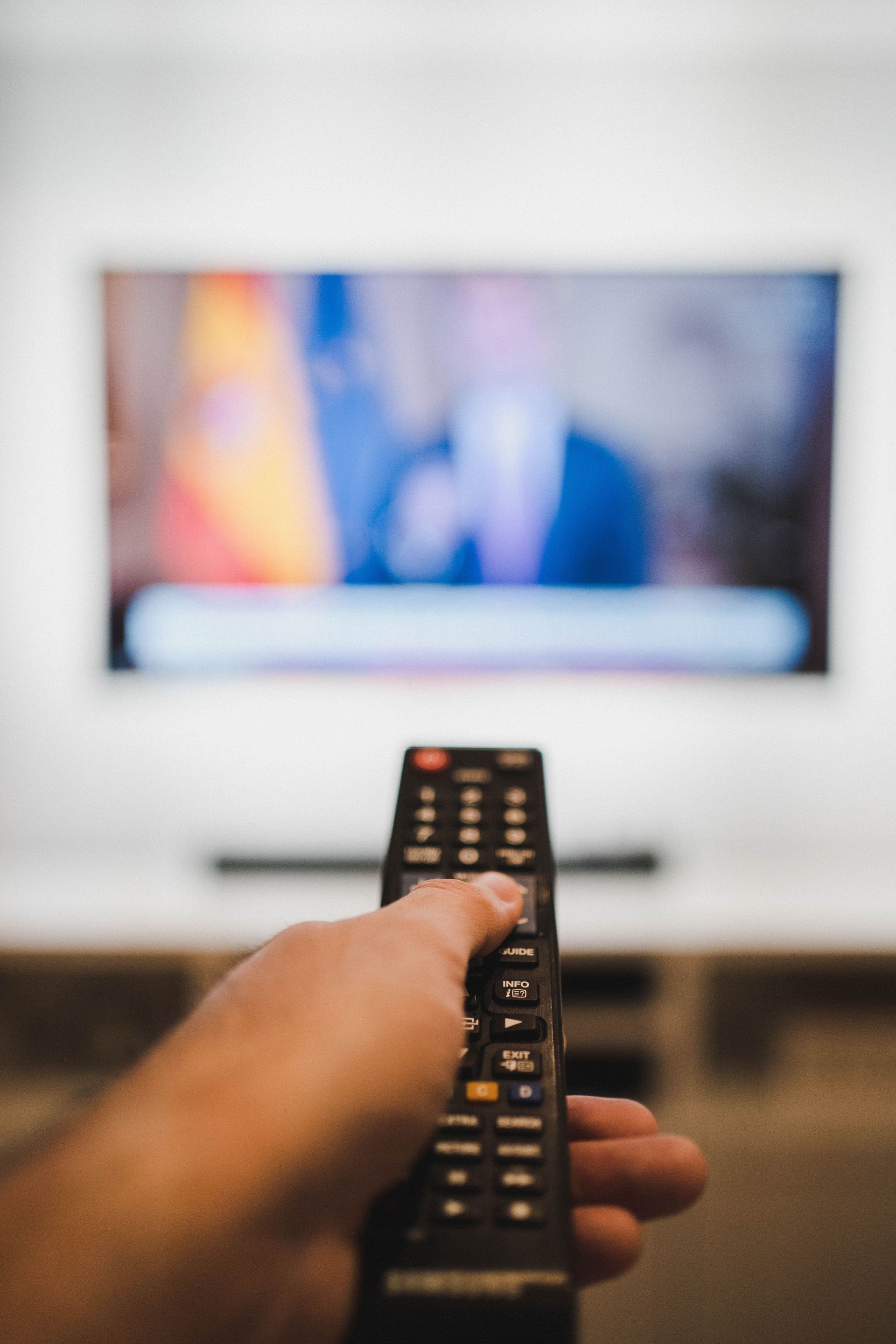Hand holding a remote toward a blurred television screen in a living room