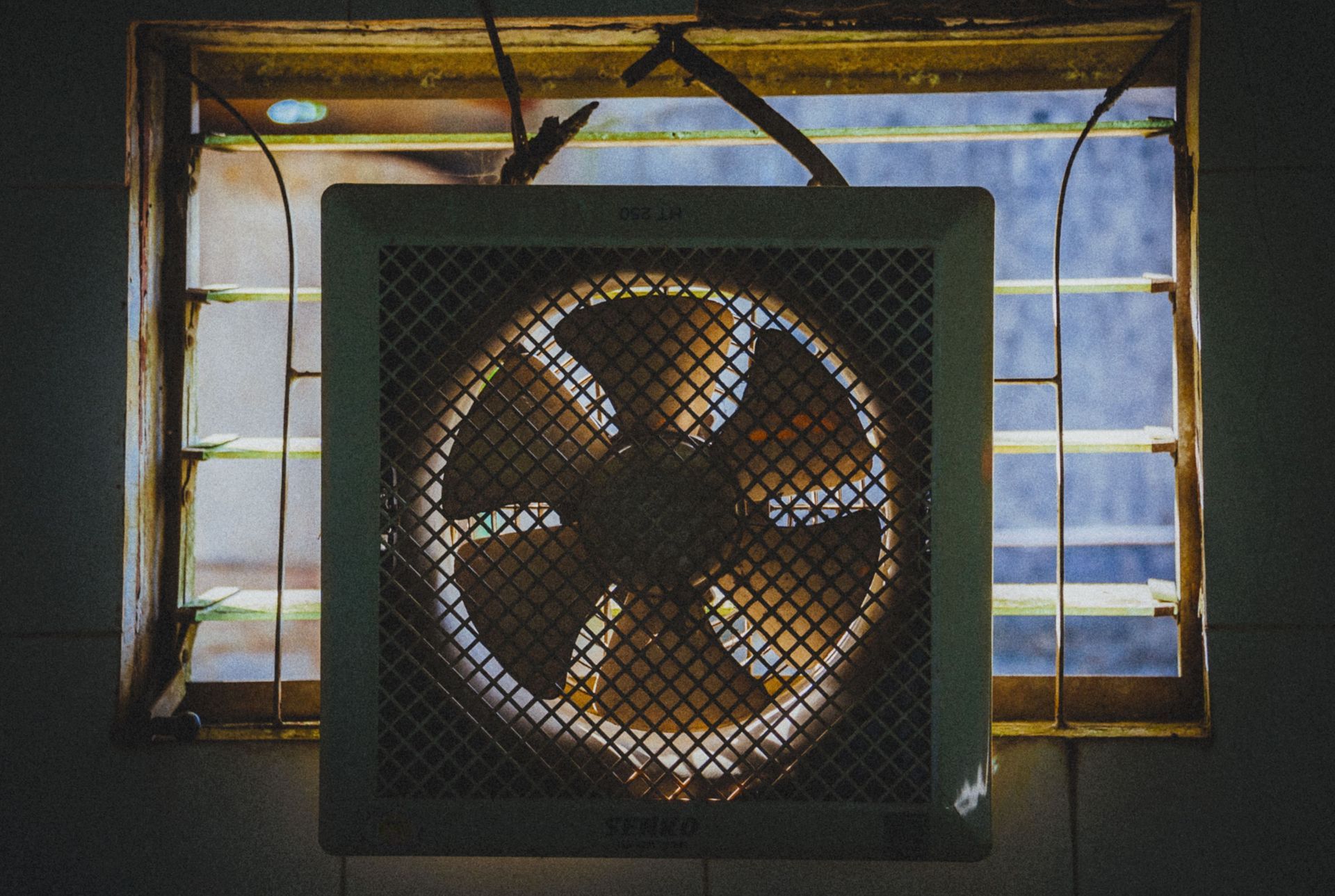 Box fan in a window with sunlight and curtains behind it