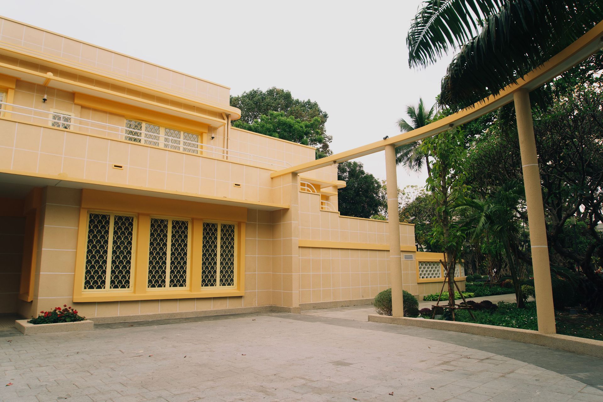 Yellow two-story house with arched windows, a driveway, and lush green trees nearby