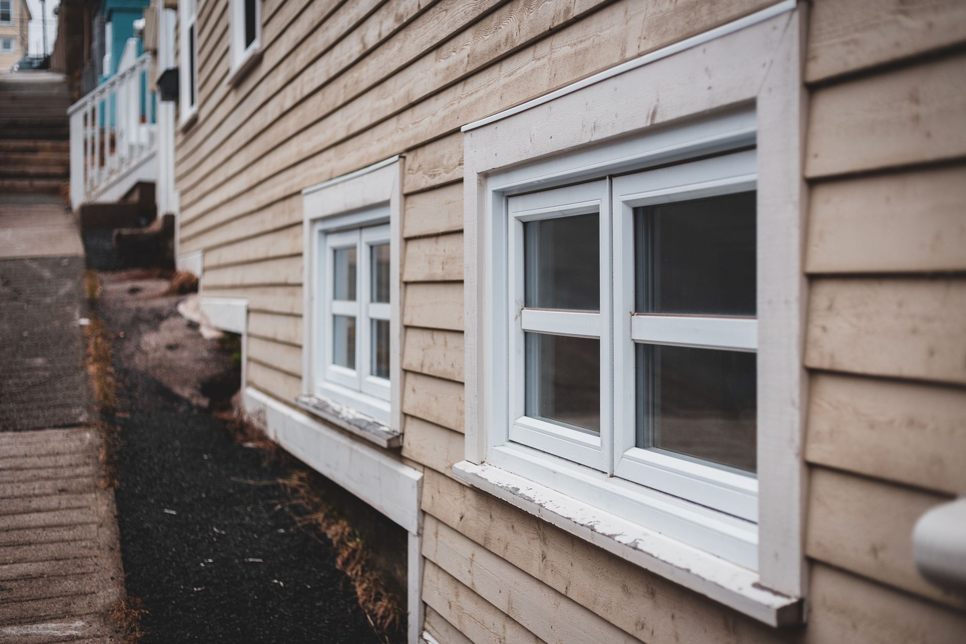 Exterior side of a beige house with white-framed windows along a narrow walkway