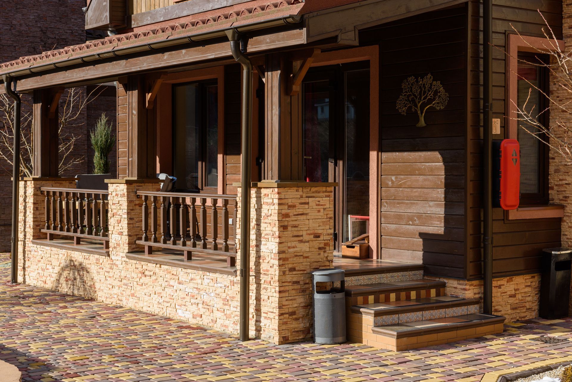 Wooden porch and stone facade of a rustic building with columns, railing, steps, and a red mailbox