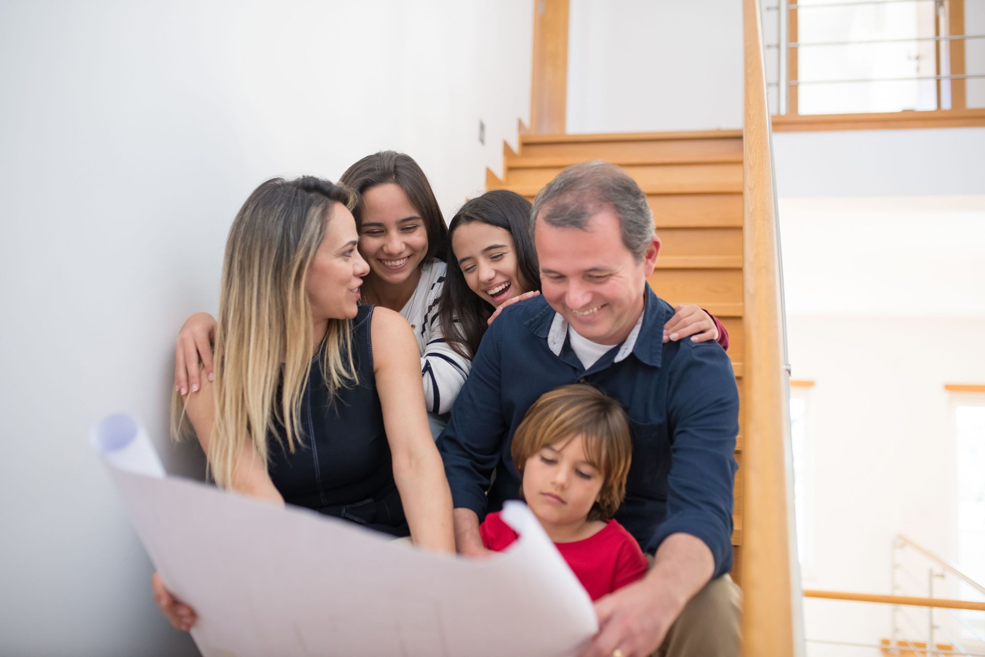 Family gathered on a staircase, smiling and looking at a large paper together