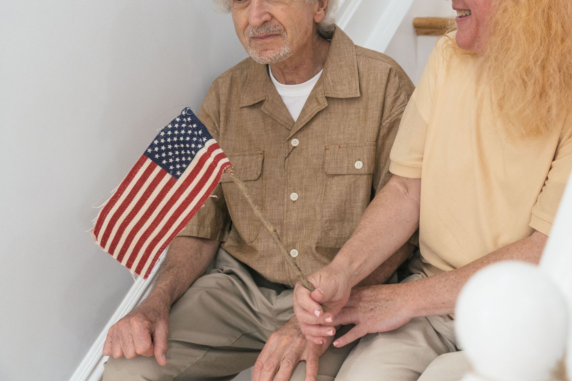 Man sitting beside another person, holding hands with an American flag nearby