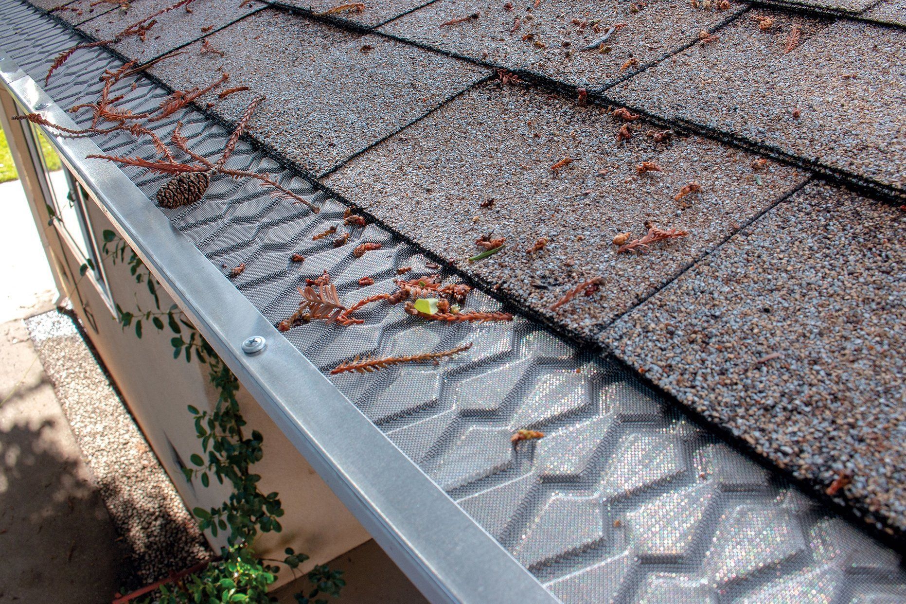 Roof shingles with a damaged ridge vent and a metal gutter lined with leaves and debris