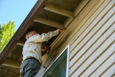 Person using a power drill to work on the exterior siding under a house eave