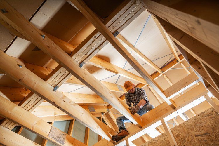 Construction worker framing a wooden roof structure inside an unfinished house