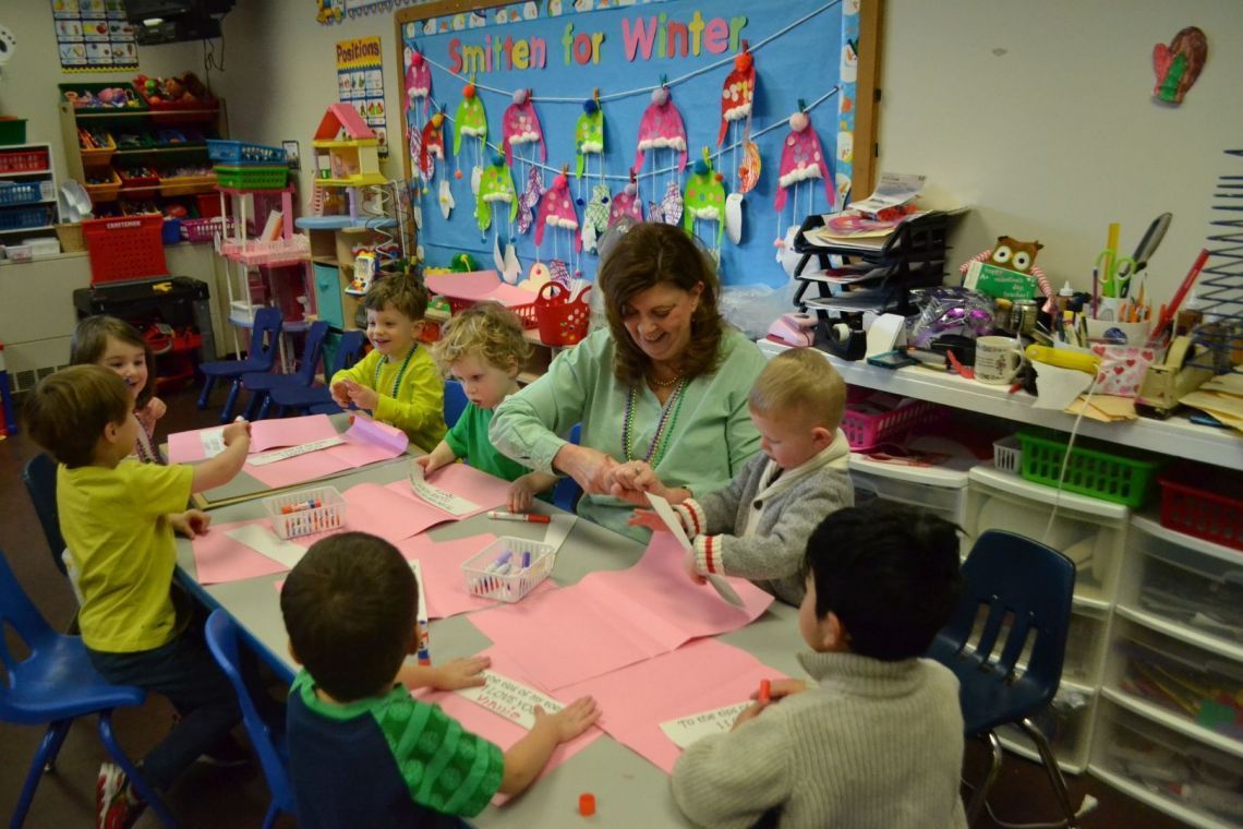 A group of children are sitting at a table in front of a bulletin board that says smiles for winter