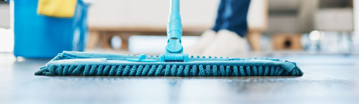 Un trapeador azul limpia un piso; un balde azul en el fondo y una persona es visible.