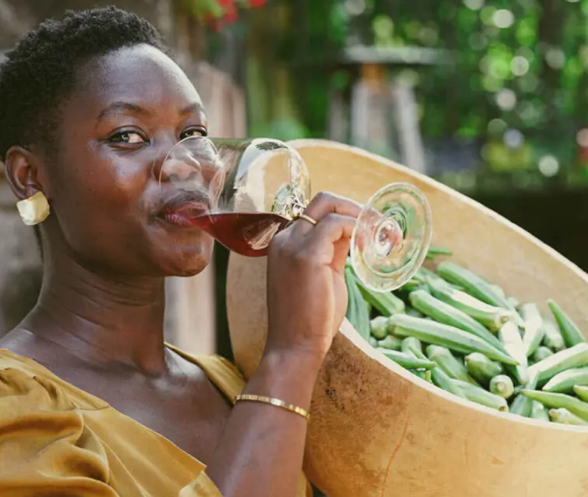 A woman is drinking a glass of wine next to a bowl of green beans