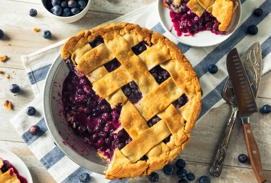 A blueberry pie with a slice taken out of it is on a table.