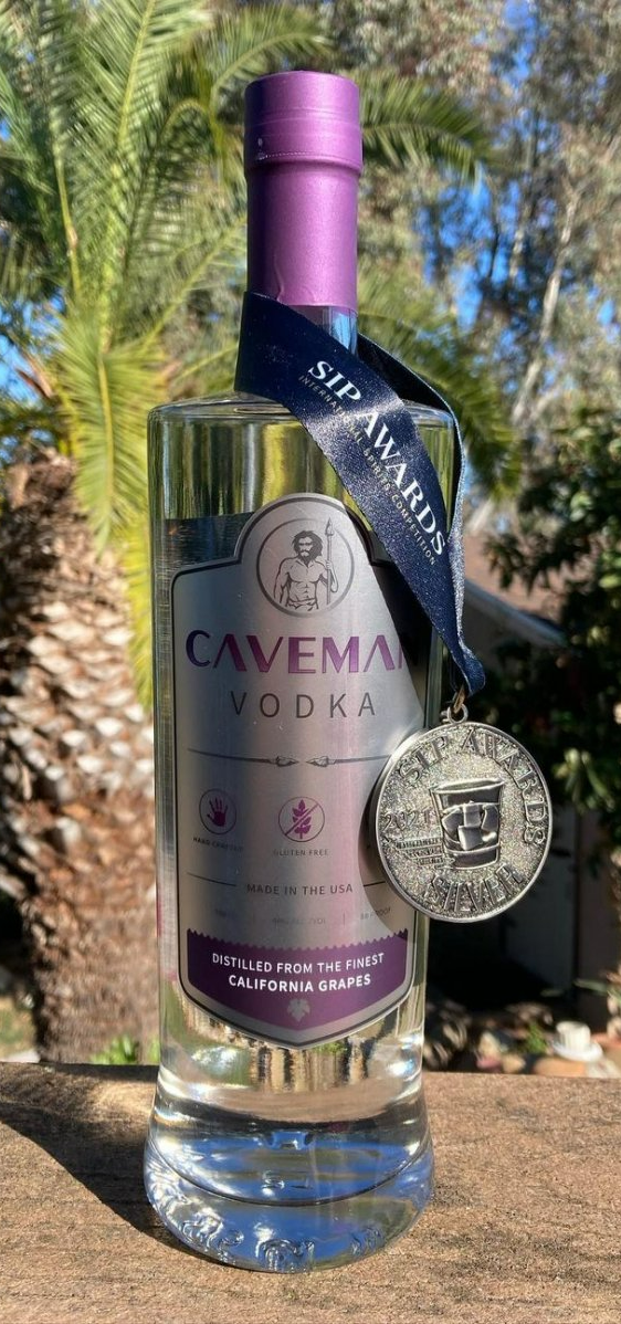 A bottle of caveman vodka with a medal on it is sitting on a rock.