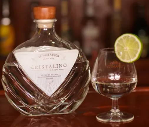 A bottle of cristalino next to a glass with a slice of lime on it