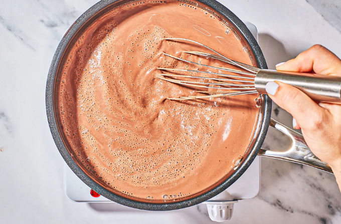 A person is whisking a pot of chocolate sauce.