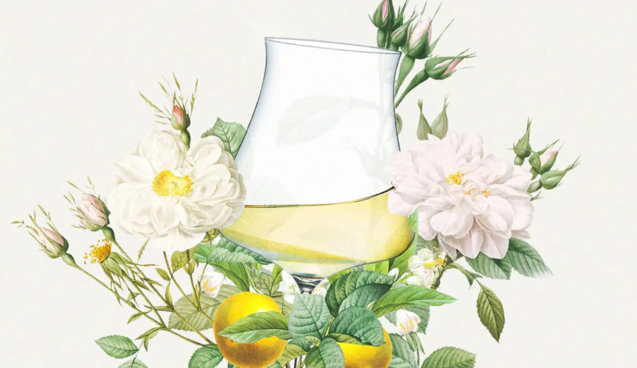 A glass of white wine surrounded by flowers and lemons.