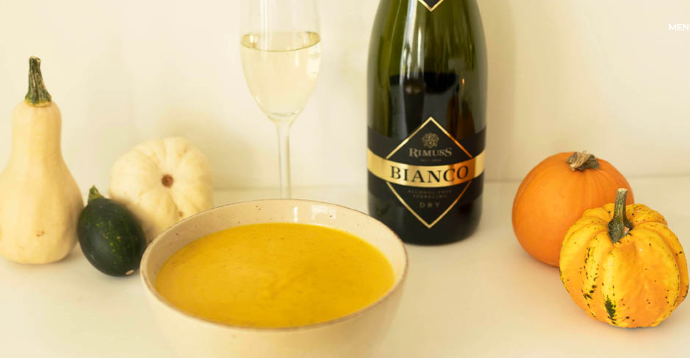 A bowl of soup next to a bottle of champagne and pumpkins.