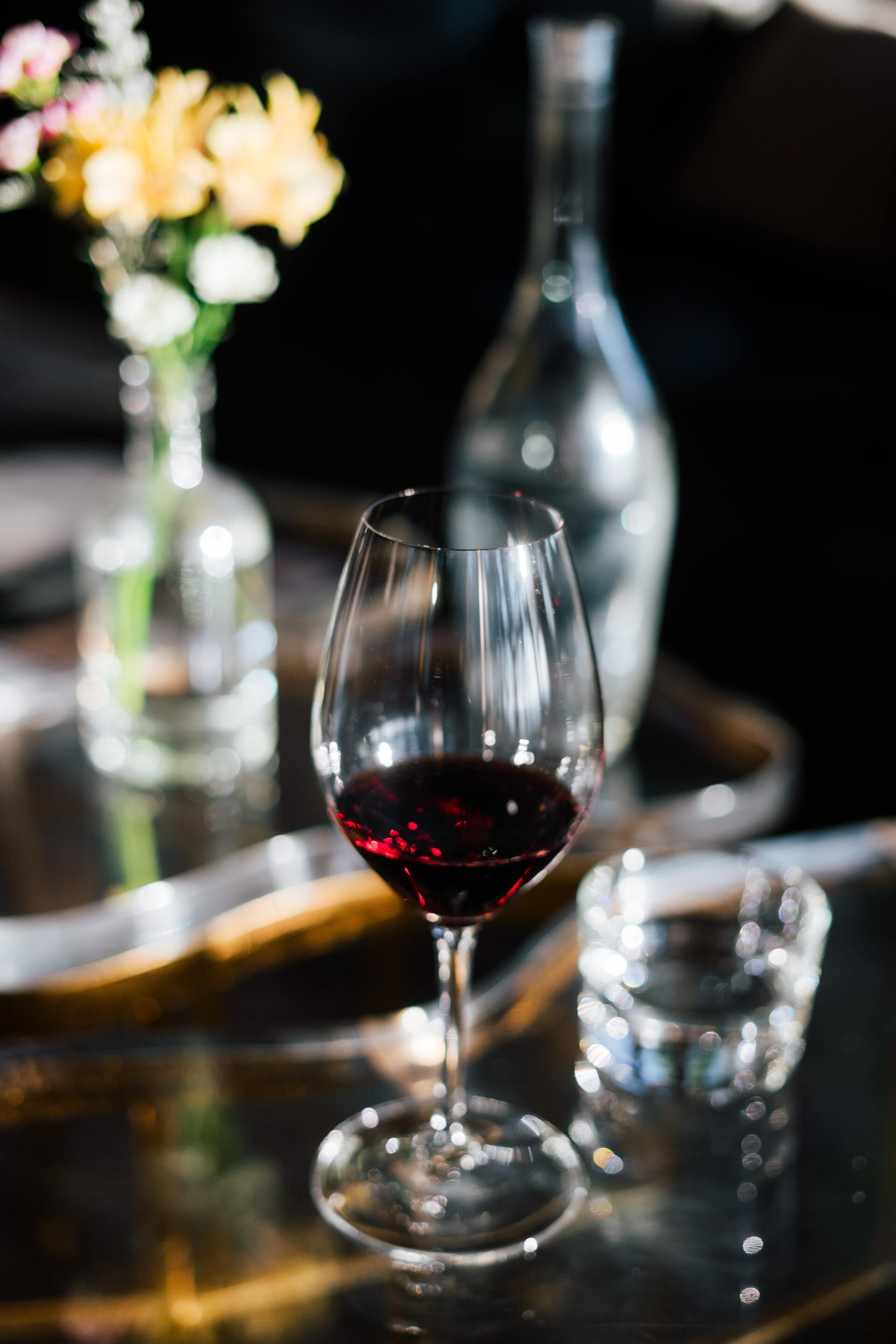 A glass of red wine is on a table next to a vase of flowers.